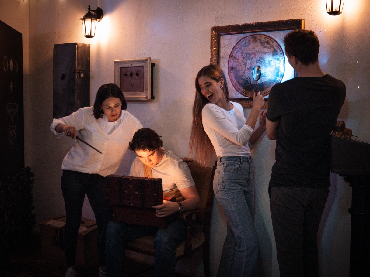 Escape Mission, Vienna, four players are in an escape room and try to solve puzzles, one participant has a laptop on his lap, one person looks at the laptop, two other participants stand against the wall and look at the laptop