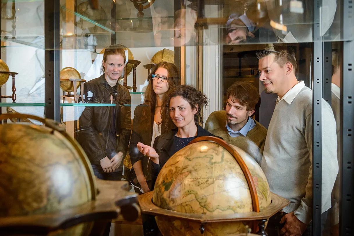 Globenmuseum, Wien, Besuchergruppe steht vor zwei großen historischen Globen, die in einer Vitriene stehen