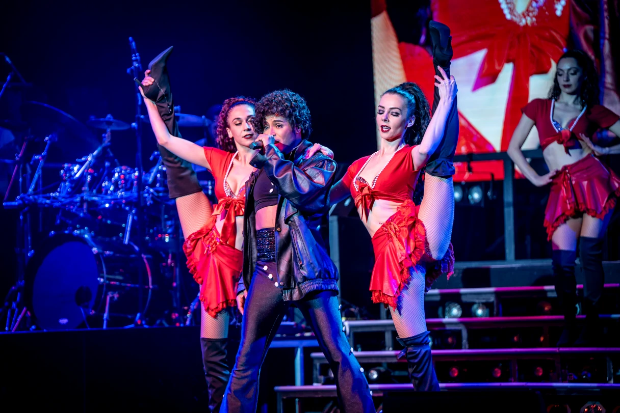 Stars in Concert. A Michael Jackson lookalike stands on the stage and is surrounded by two dancers, each holding up one leg to do the splits. Another dancer comes running down the show stairs in the background.