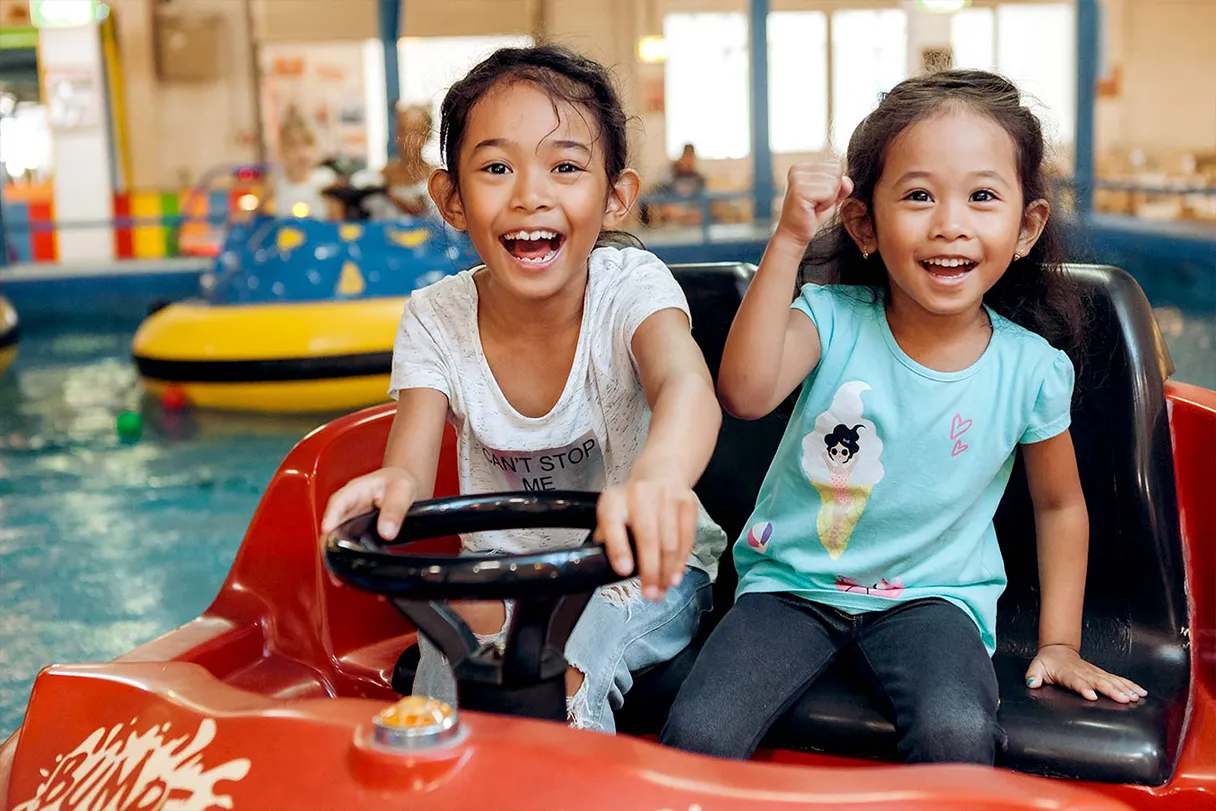 Family Fun, Indoor-Spielplatz, zwei Mädchen fahren auf einem Wasserfahrzeug und freuen sich, lachen in die Kamera