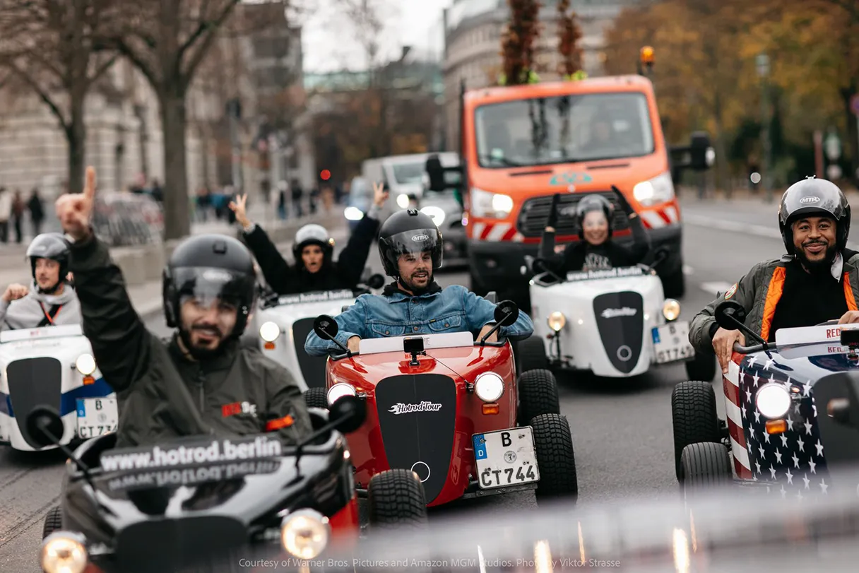 Hotrod tour along the road. Drivers throw their arms up in the air and have fun.