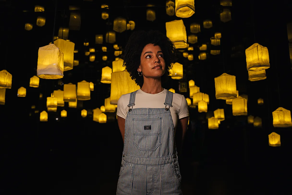 IKONO Berlin, woman walking through a dark room, yellow lanterns hanging from the ceiling