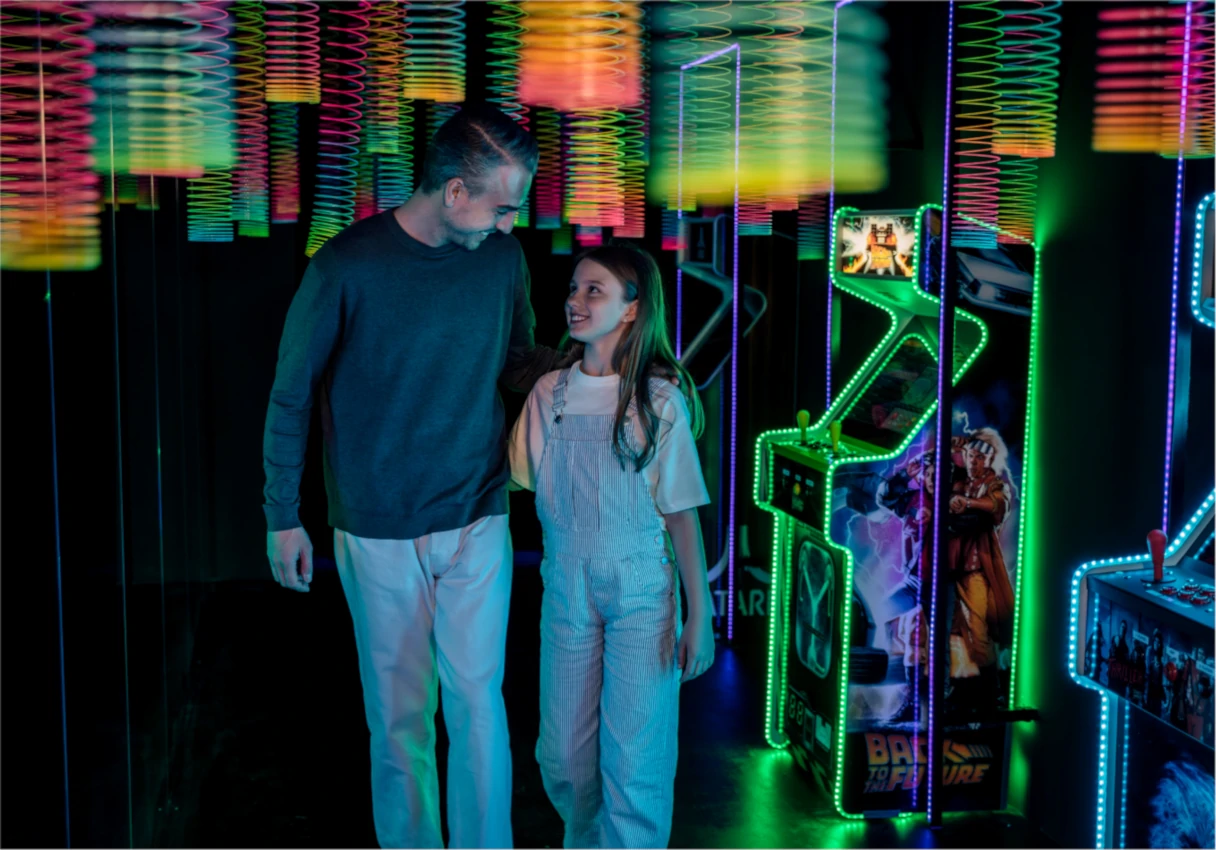 IKONO Vienna, father and daughter walk through the museum, it is dark around them, neon-colored elements stand at the edge and hang from the ceiling