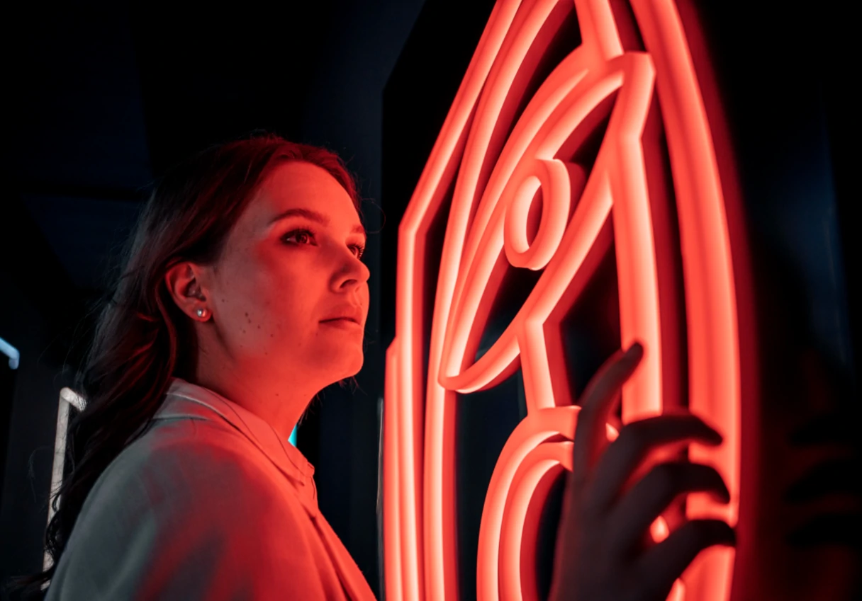 IKONO Vienna, woman standing at a red neon sign and looking diagonally past the neon sign