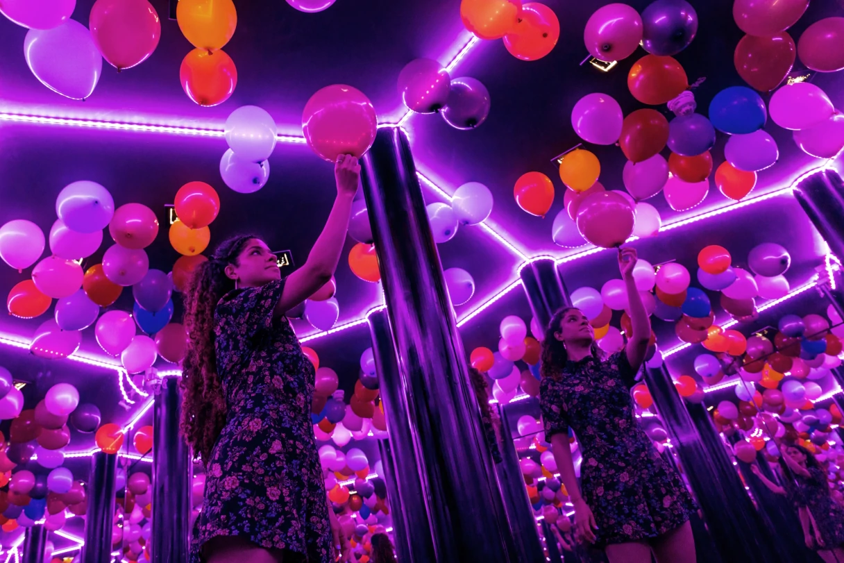 Illuseum Berlin, Infinity Room, Frau steht in einem Raum der unendlich groß zu sein scheint, lila, pinke Luftballons