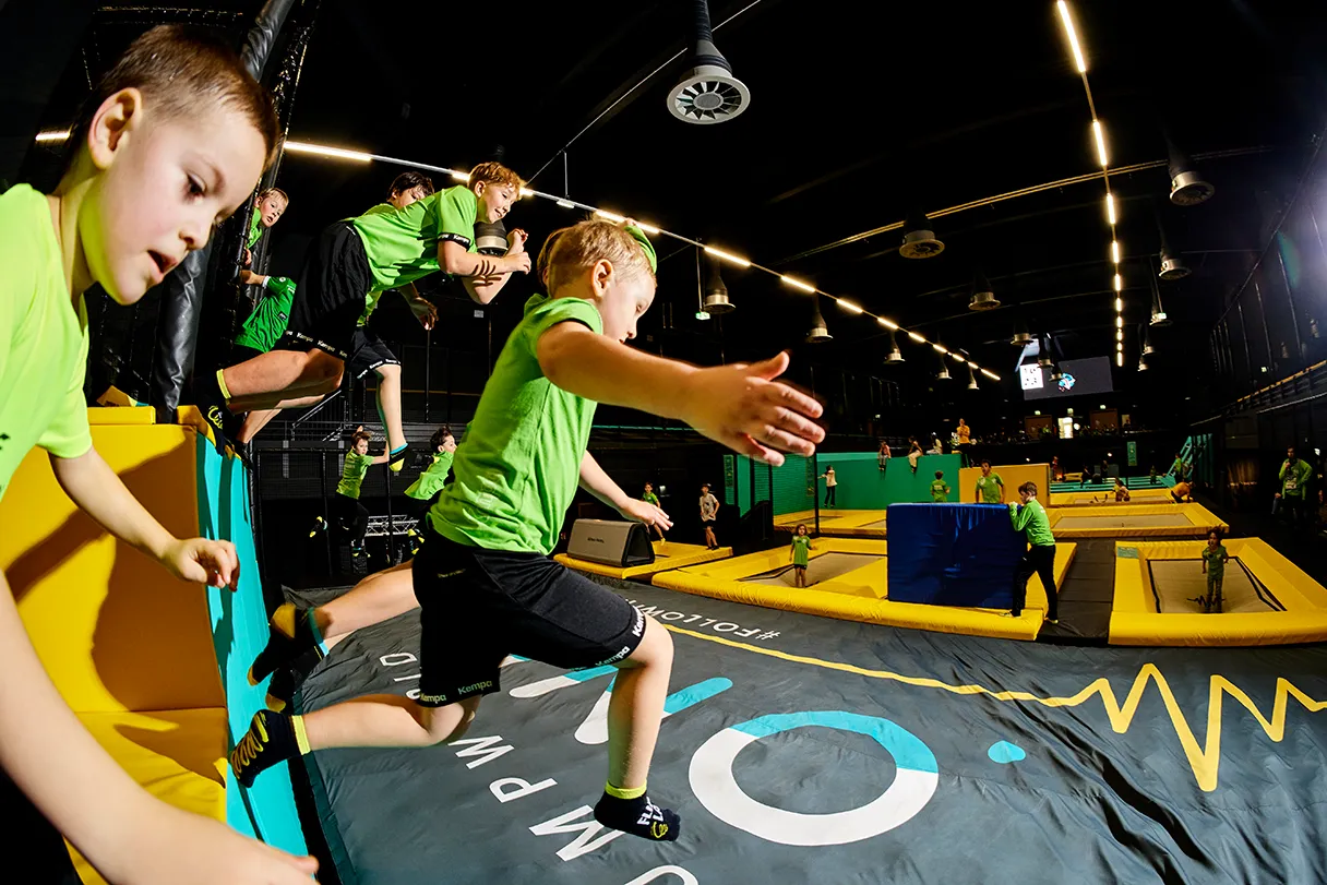 Jumpworld One, several boys in green T-shirts and black pants jump from the top down onto a trampoline