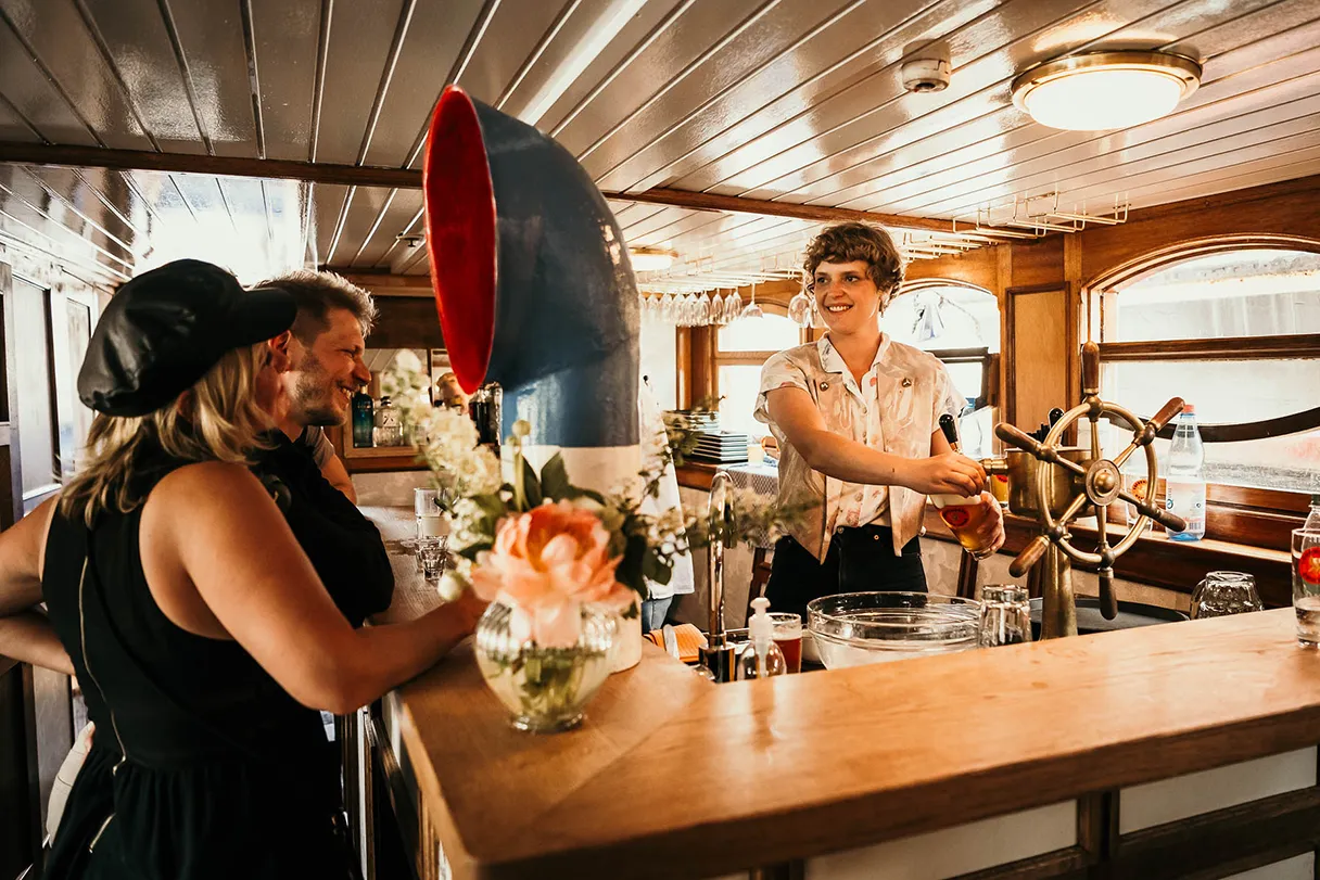 Kaiser Friedrich, Schiff, Berlin, unter Deck an der Bar, Gäste stehen am Tisch und unterhalten sich mit der Barfrau, die gerade ein Bier zapft und lachen