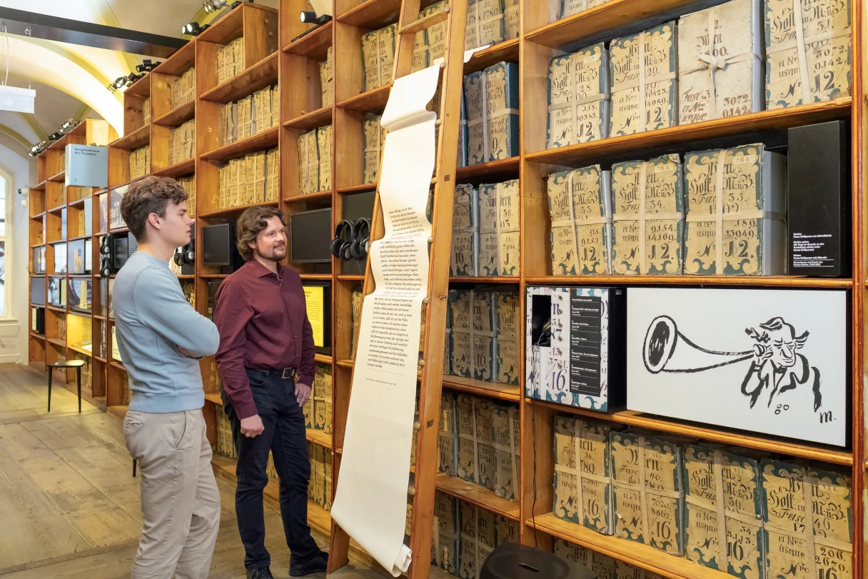 Literaturmuseum Wien. Zwei Männder stehen vor Regalen, die mit verschiedenen literarischen Werken gefüllt sind und lesen sich Erklärungen durch.