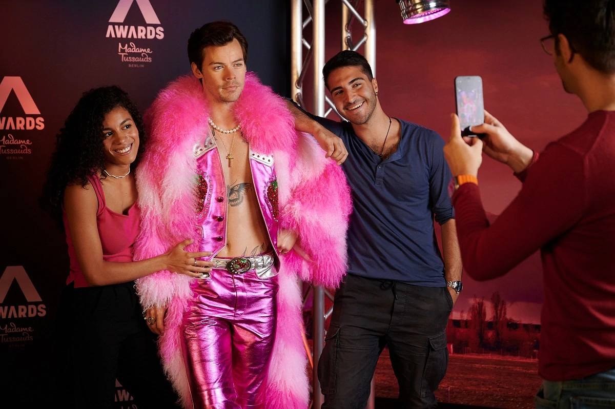 Madame Tussauds Berlin, Wachsfiguren, Harry Styles in rosafarbenen Klamotten wird von zwei Besuchern umrahmt, die ein Selfie mit ihm machen