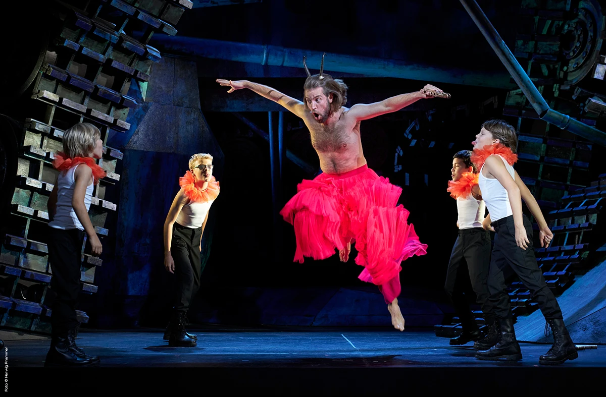 MusikTheater an der Wien - Kammeroper, Bühnenbild, Künstler springt mit ausgebreiteten Armen und pinker Hose zwischen anderen Künstlern in die Luft