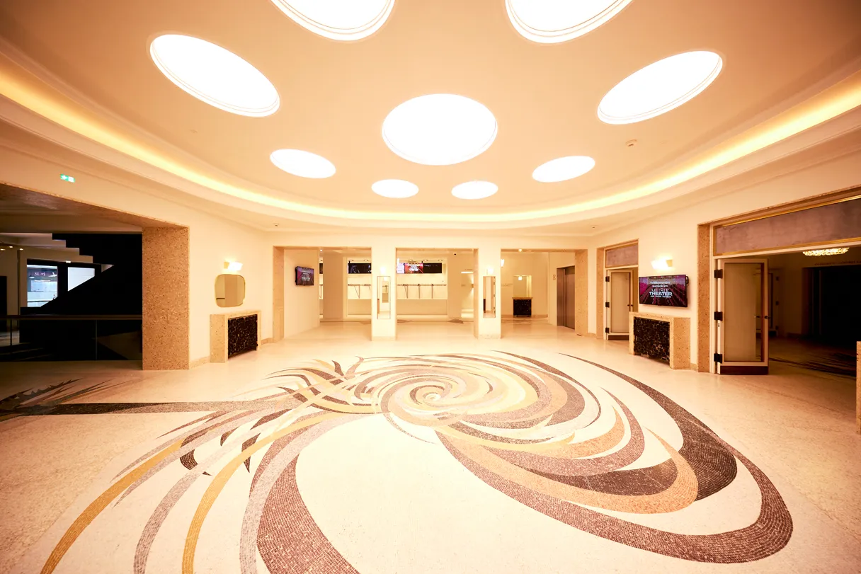 View of the foyer in the Theater an der Wien. Elaborate floor mosaics and round ceiling lights.