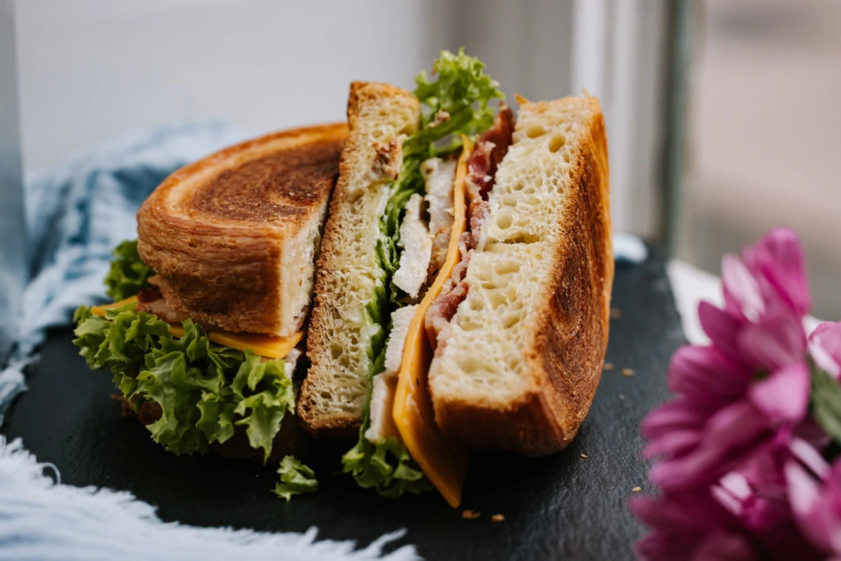 New York Rolls, Wien, ein herzhaft belegtes New York Roll liegt aufgeschniten auf einer Schiefertafel, am rechten Rand sind pinke Blumen unscharf zu erkennen