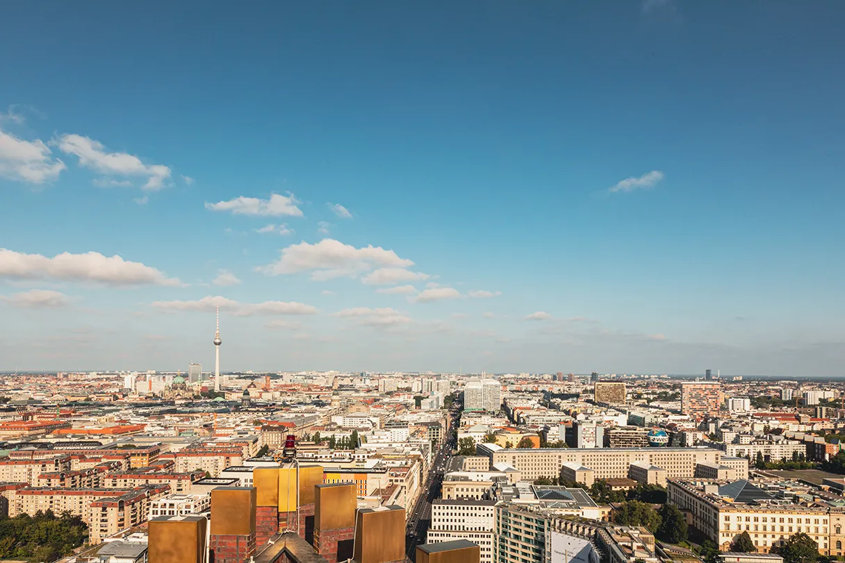 Blick vom Panoramapunkt über Berlin. Blauer Himmel, Sonnenschein, ein paar weiße Wolken. Man erkennt den Fernsehturm und viele weiße Häuser und Straßen.