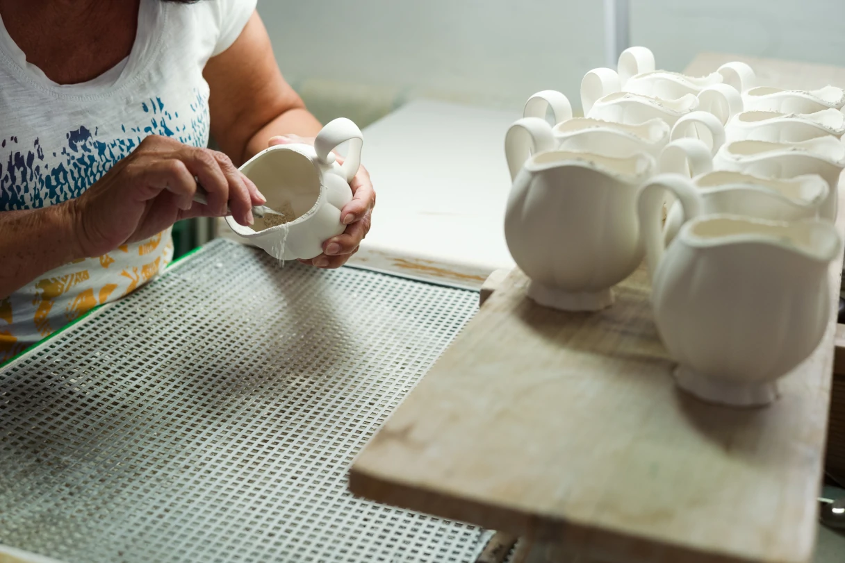 An employee of the Augarten porcelain manufactory in Vienna is sitting at her workstation. She has a board with white carafe blanks in front of her, which she is painting and working on one by one.