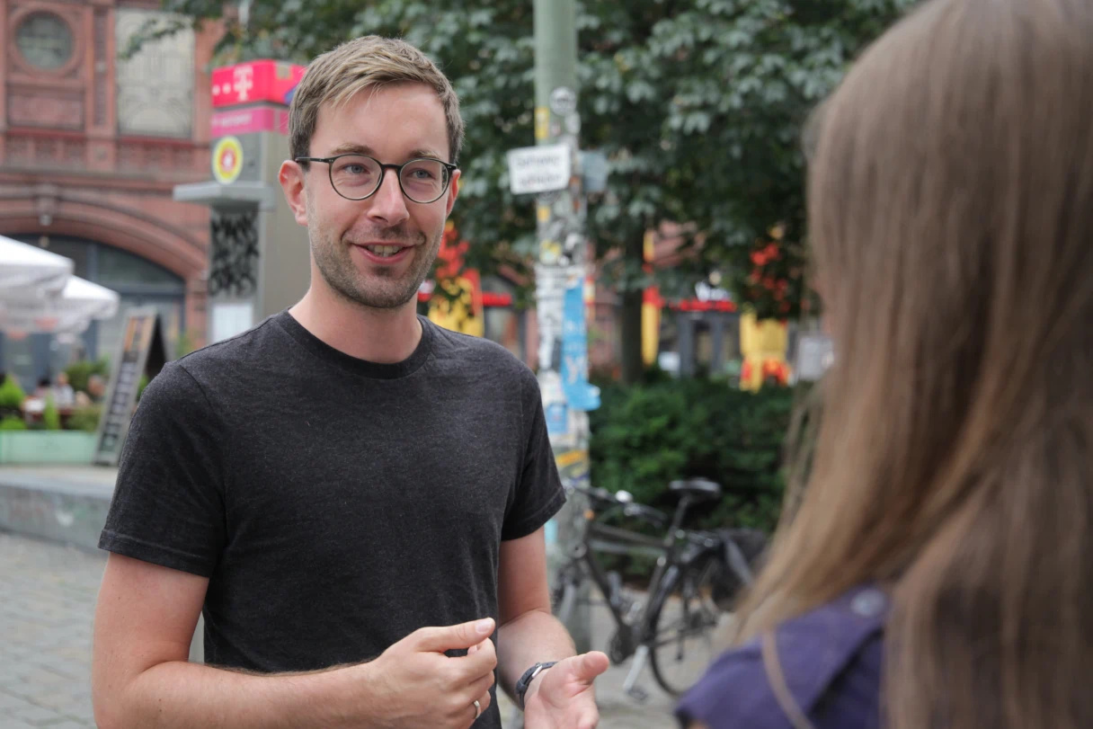 Stadtführer Matti spricht mit einer Frau, Hackescher Markt, Berlin, Mann im schwarzen T-Shirt