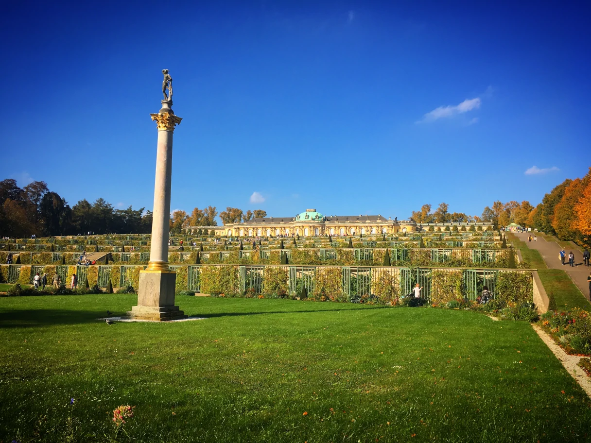 View of Sanssouci Palace in Potsdam, sunny day, blue sky, green meadow, obelisk on the left edge of the picture