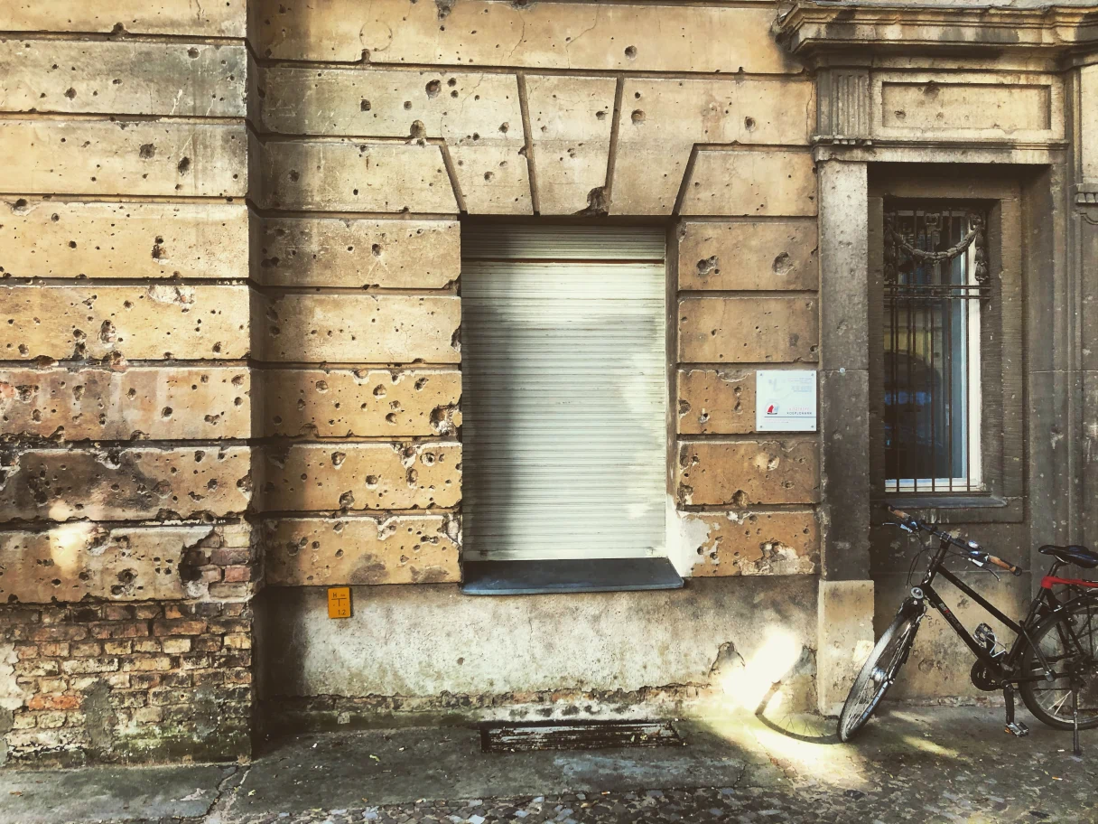 Broken old building façade, bullet holes from the Second World War can be seen, windows, bicycle on the wall of the house