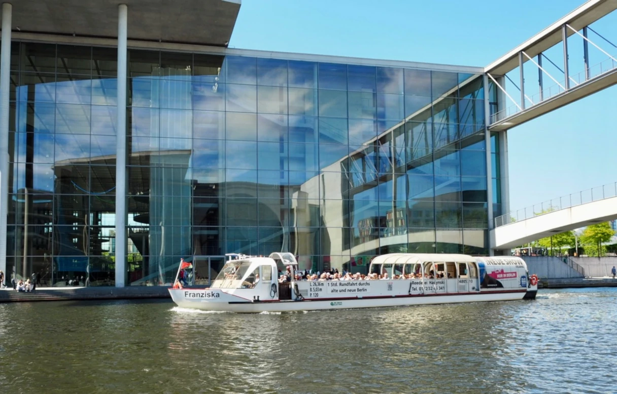 Reederei Hadynski, Berlin, Regierungsgebäude mit Glasfassade und davor fährt ein Schiff, Brücke