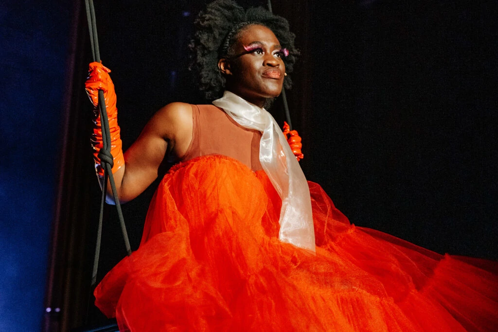 Ivy Quainoo sitzt in einem orangenen Tüllkleid auf einer Schaukel