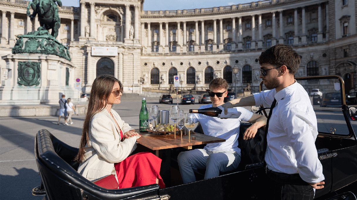 Ring Tours Vienna vor der Hofburg Ring Tours Vienna vor der Hofburg Wien. Ein Paar sitz im Oldtimer und bekommt gerade den Prosecco in die Gläser eingegossen.