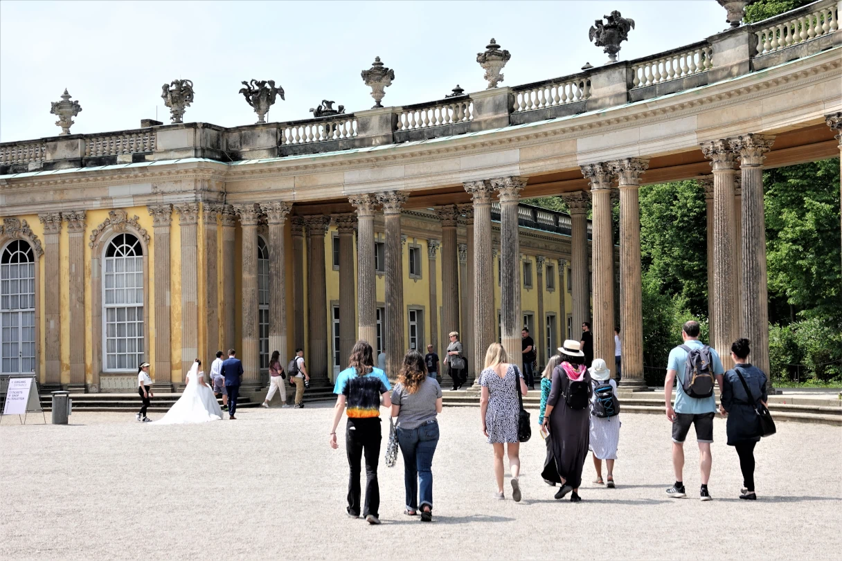 Schloss Sanssouci, Potsdam, blauer Himmel, Sonnenschein, Menschen laufen vor dem Schloss entlang