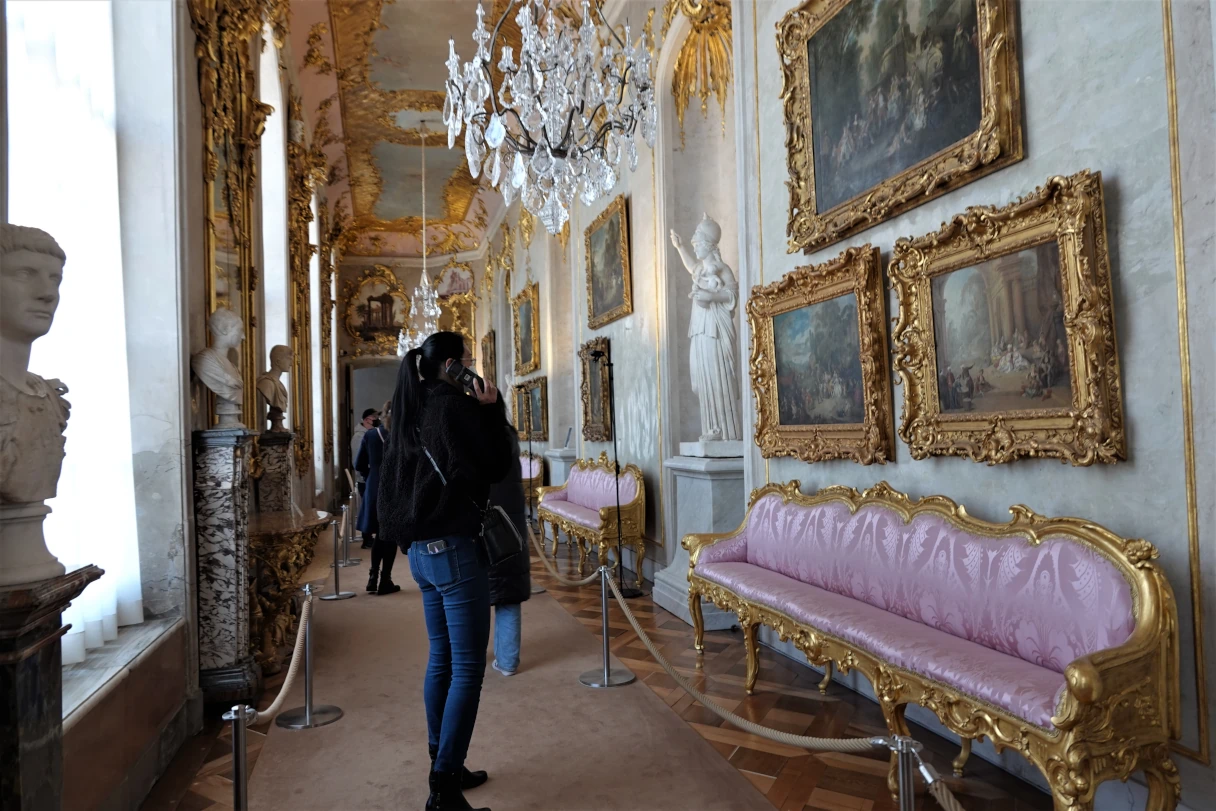 Schloss Sanssouci, Potsdam, im Inneren des Schlosses, Frau hält sich einen Audioguide ans Ohr und schaut sich Gemälde an, die an einer Wand hängen, prunkvoll