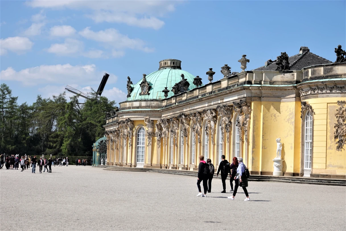 Schloss Sanssouci, Potsdam, blauer Himmel, Sonnenschein, Menschen laufen vor dem Schloss entlang