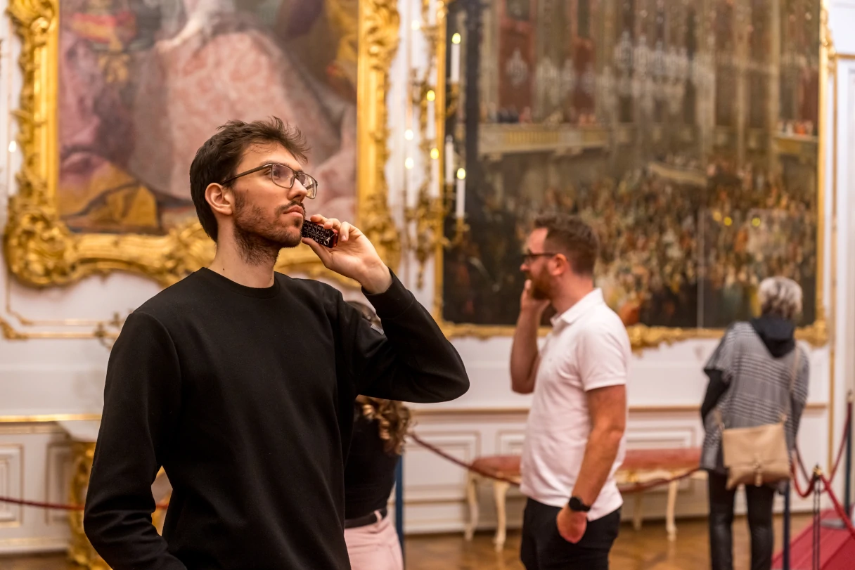 Schloss Schönbrunn Wien, Besucher schauen sich in den prunkvollen Räumlichkeiten um, hören einen Audioguide, große Gemälde hängen an der Wand