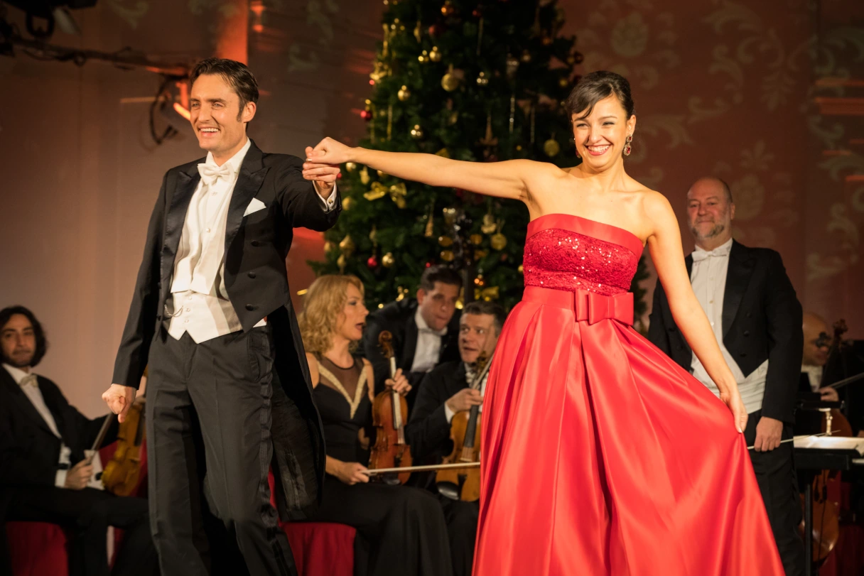 Schloss Schönbrunn Konzerte, Sängerin in rotem Kleid und Sänger im Frack stehen auf der Bühne und verbeugen sich