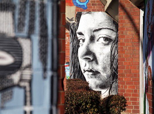 Street art, woman face peeping out of a house wall
