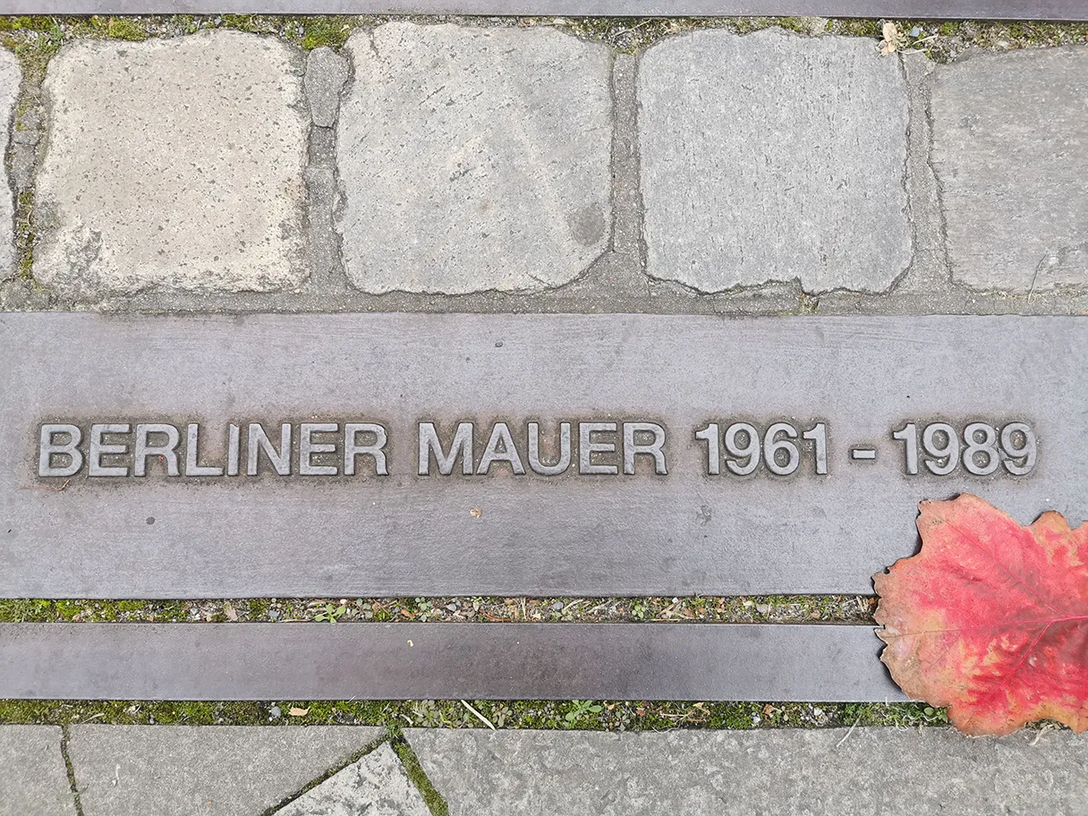 Berlin Wall, sign embedded in ground, red autumn leaf at right edge of picture