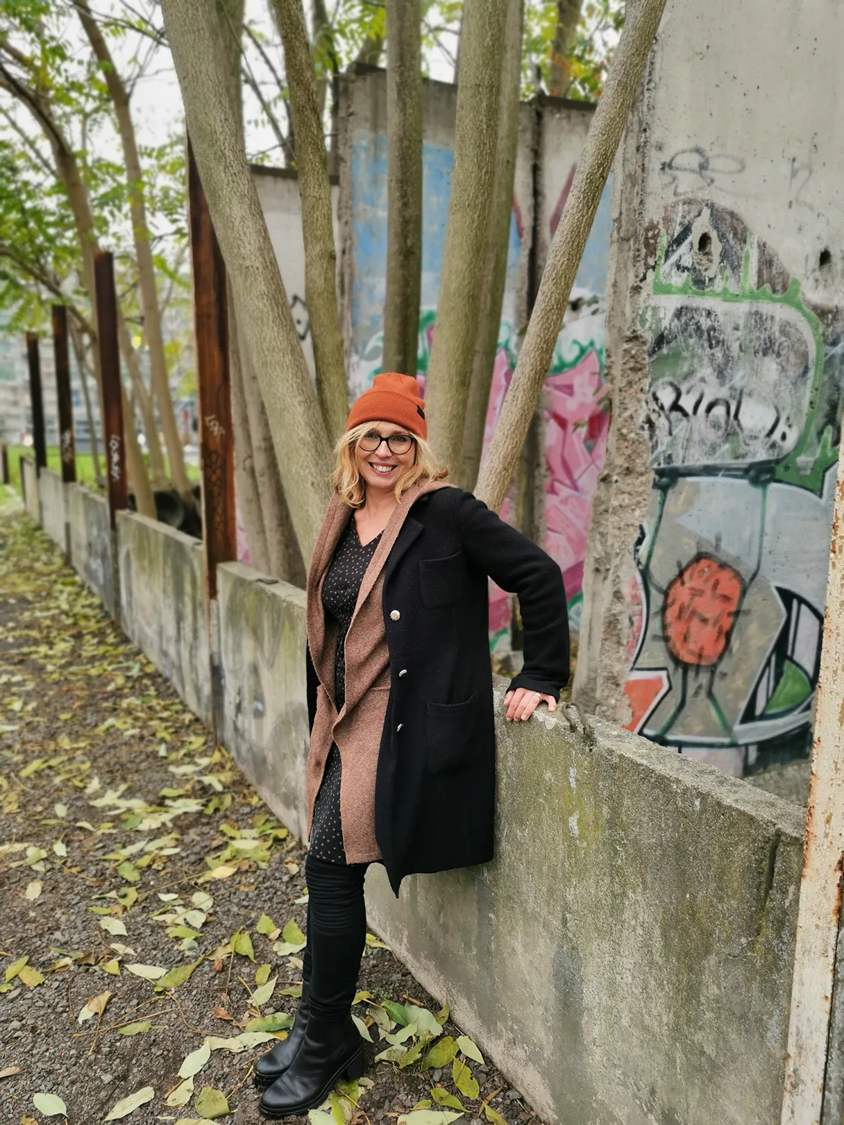 Birigit L., Berliner Mauer, Birgit lehnt an einem Stück Mauer und lächelt in die Kamera