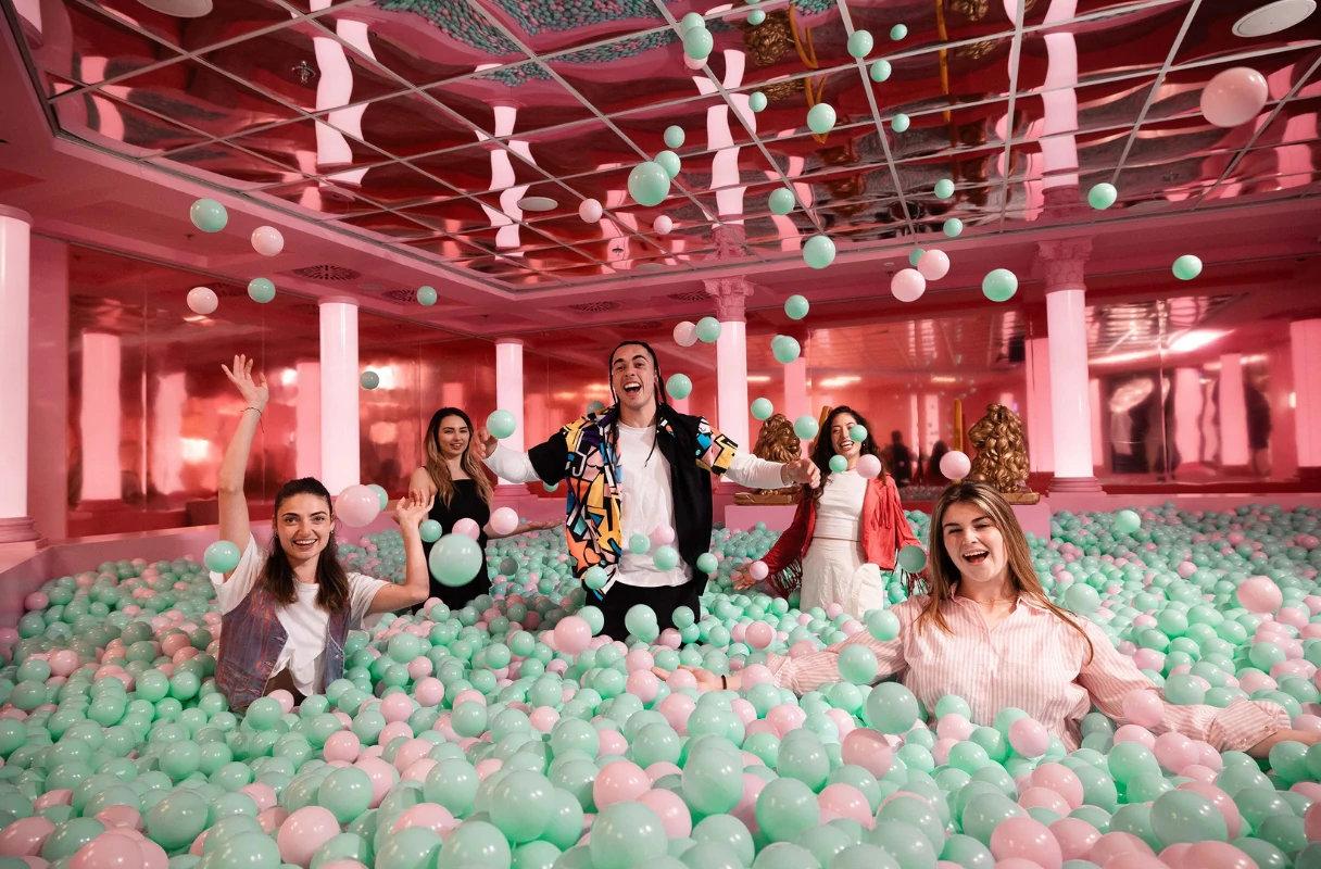 The Upside Down Berlin, five people sitting in a rose-green ball pool, throwing balls in the air, having fun together