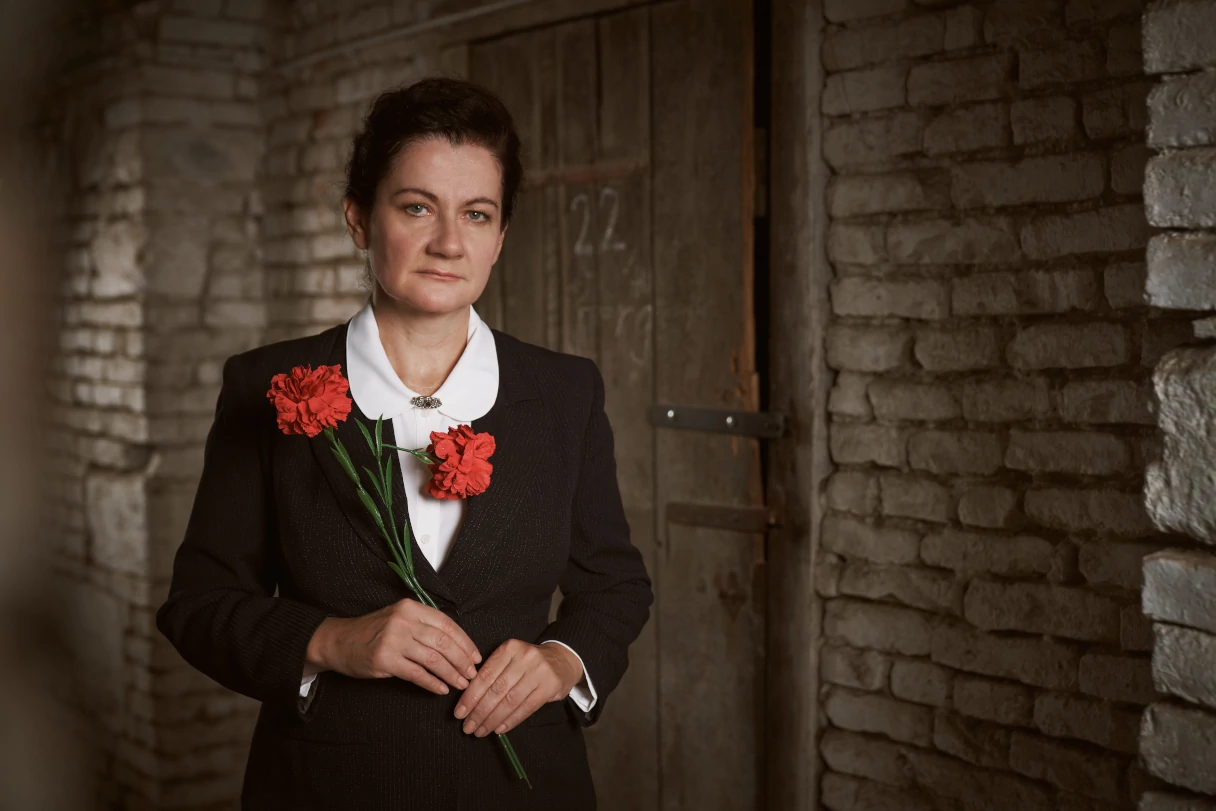 Theater Drachengasse, Wien, Frau mit schwarzem Jacket, weißer Bluse und zwei roten Nelken in der Hand steht in einem Kellergewölbe und schaut in die Kamera