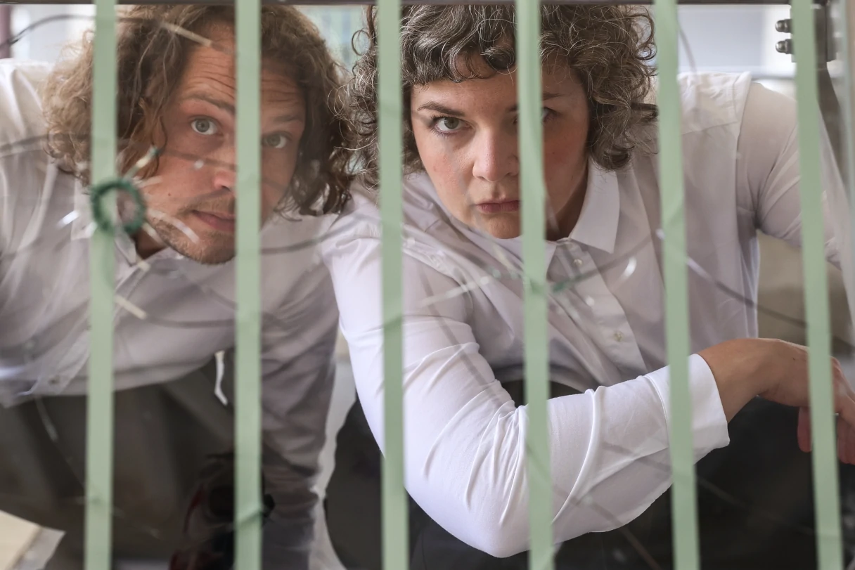 Theater Drachengasse, Vienna, a woman and a man in white shirts and gray pants look through green bars