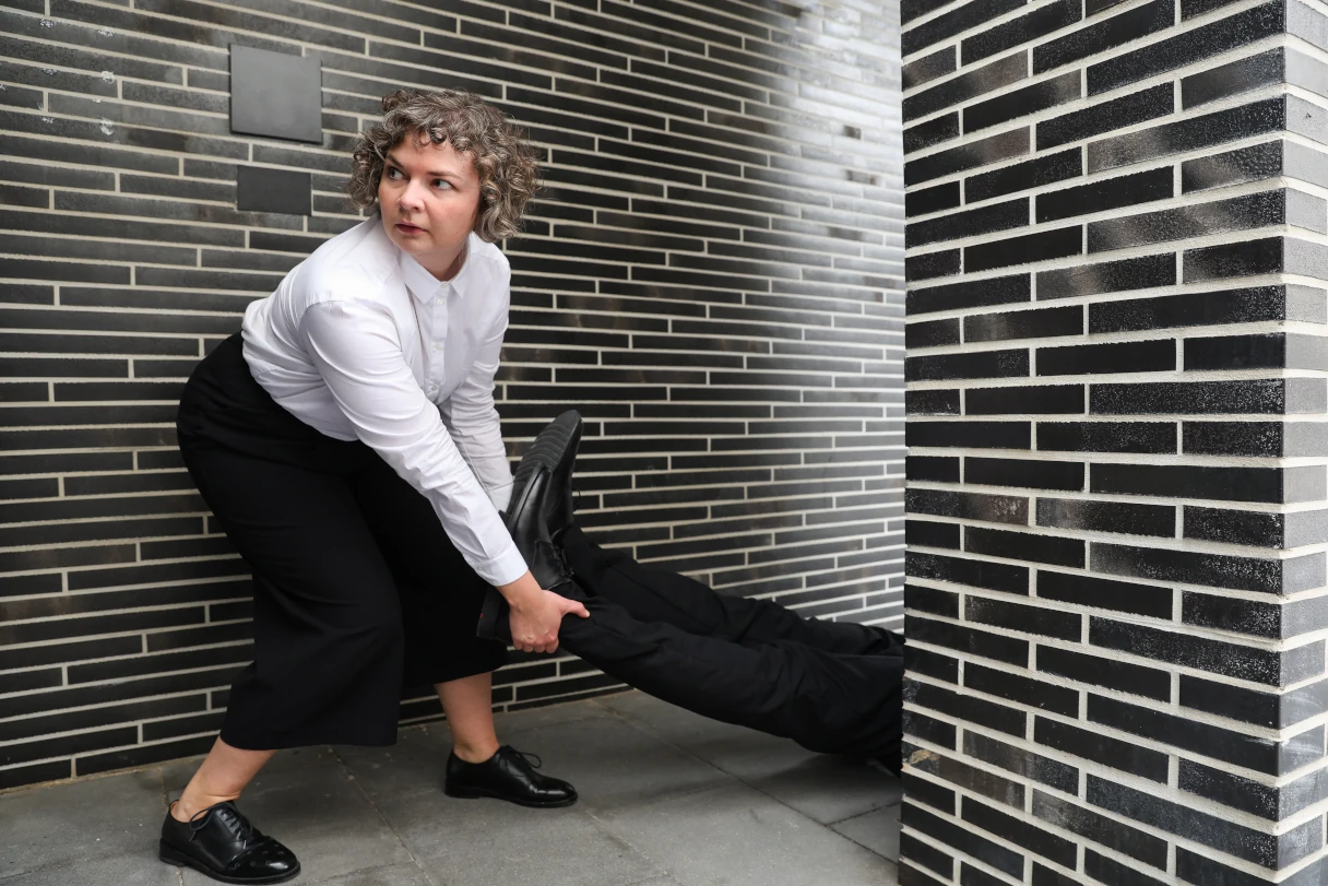 Theater Drachengasse, Vienna, woman in white blouse and black trousers drags a person behind a wall by her feet