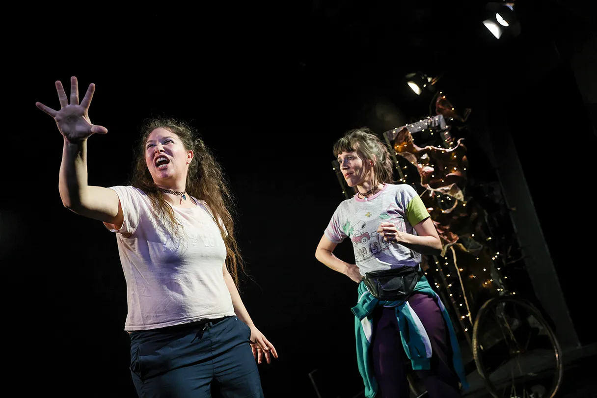 Play “DIE DÜNTZER RHAPSODIE” at Theater Drachengasse. Two women stand on the stage, black background. One woman screams and raises her hand.