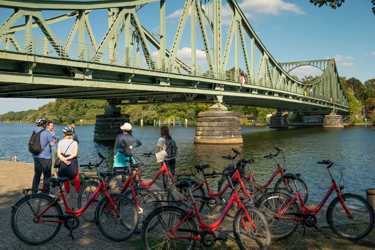 6 people on a large bridge by a river in Potsdam. Next to them are many red bicycles