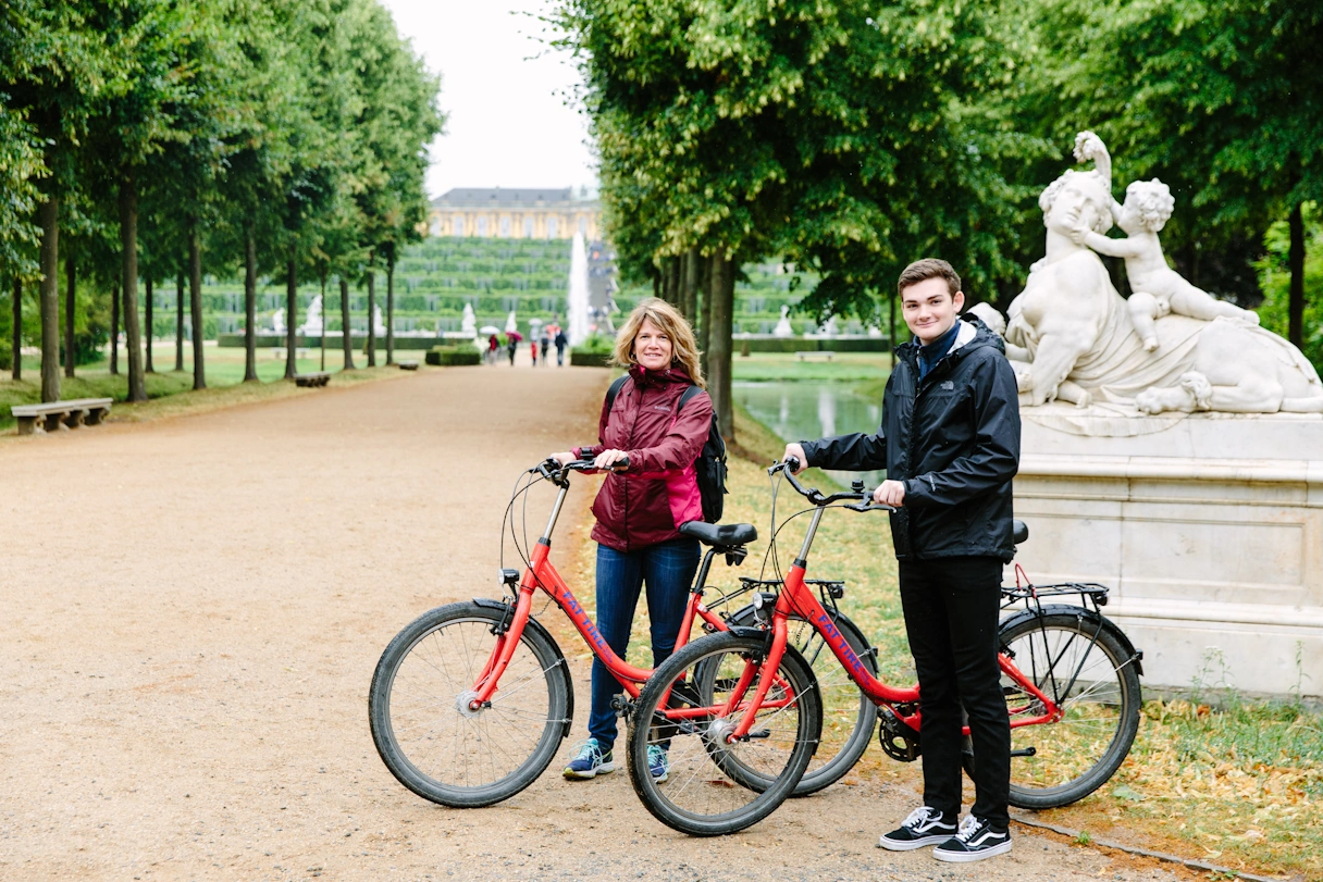 A woman and a young man are riding red bicycles in Sanssouci Park.