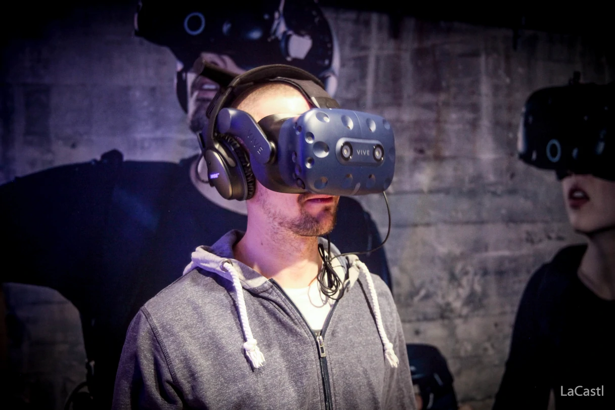 Virtual Escape Room, man has virtual reality glasses on and looks into the room, in the background is a wallpaper where people with these glasses can also be seen