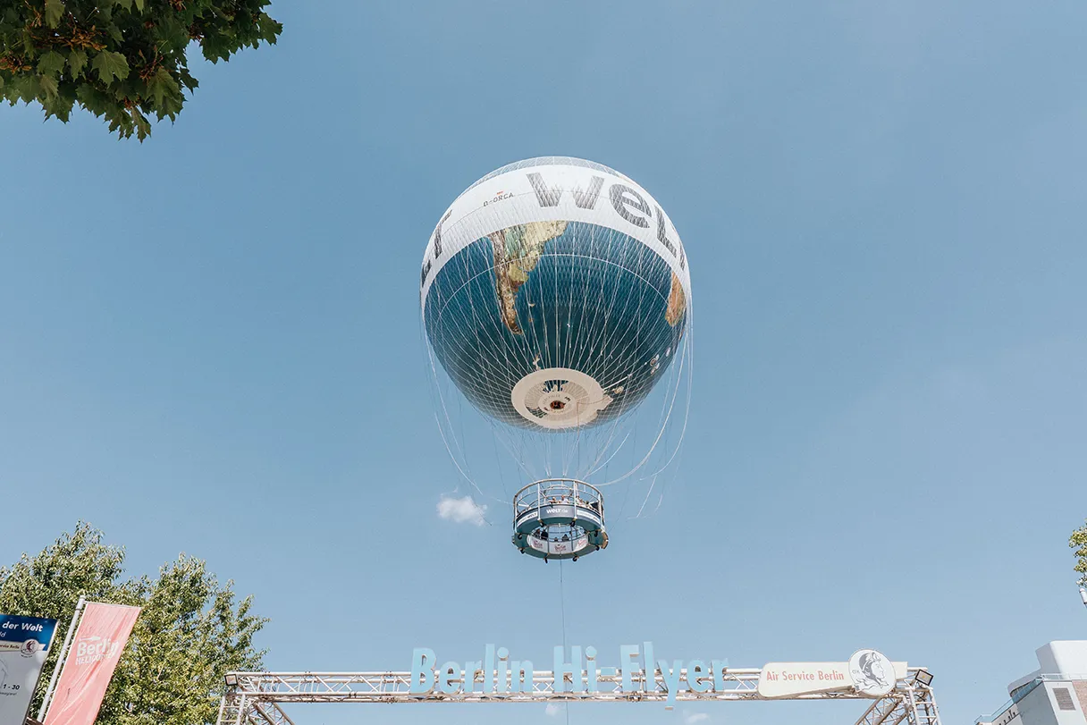 Weltballon Berlin, schwebt in der Luft, es ist Berlin Hi-Flyer vom Eingangsbereich zu lesen, sonniger Tag, blauer Himmel