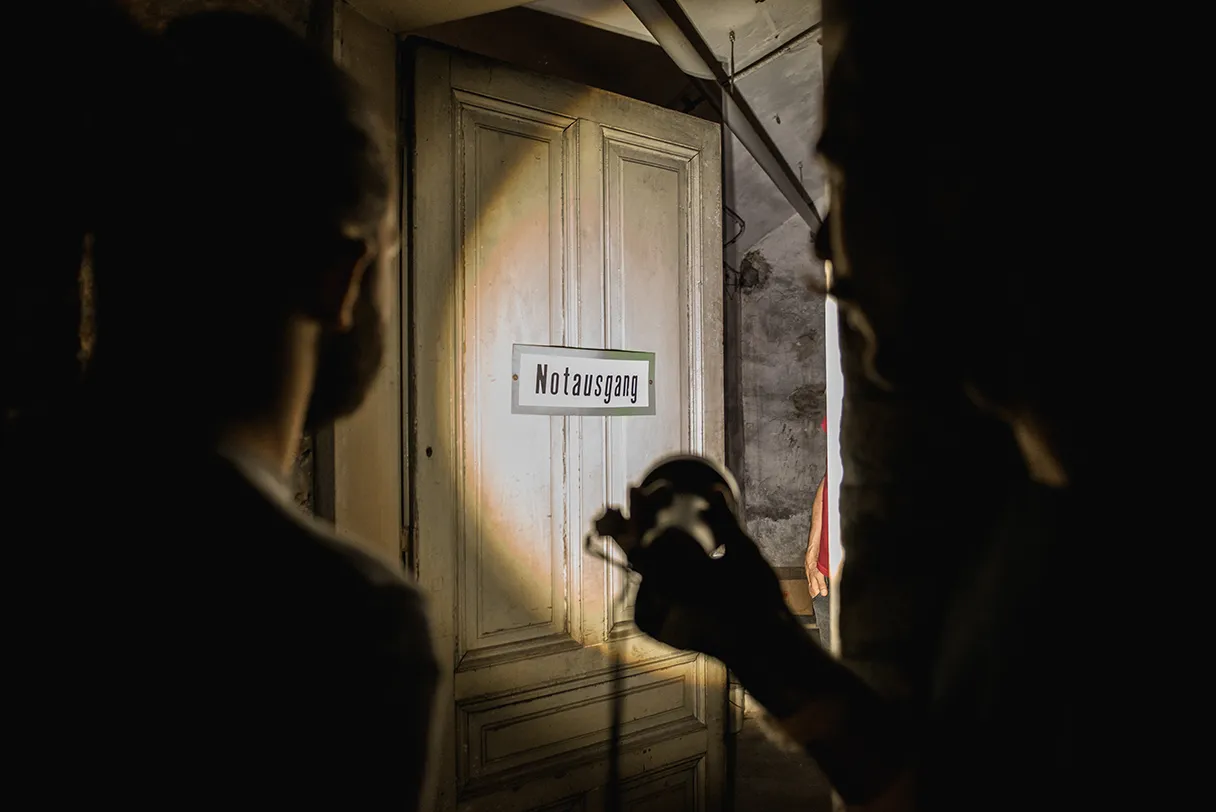 Wien mal anders, Tour in die Wiener Unterwelt, Taschenlampe leuchtet in einem dunklen Keller auf eine Tür mit einem Schild wo Notausgang drauf steht
