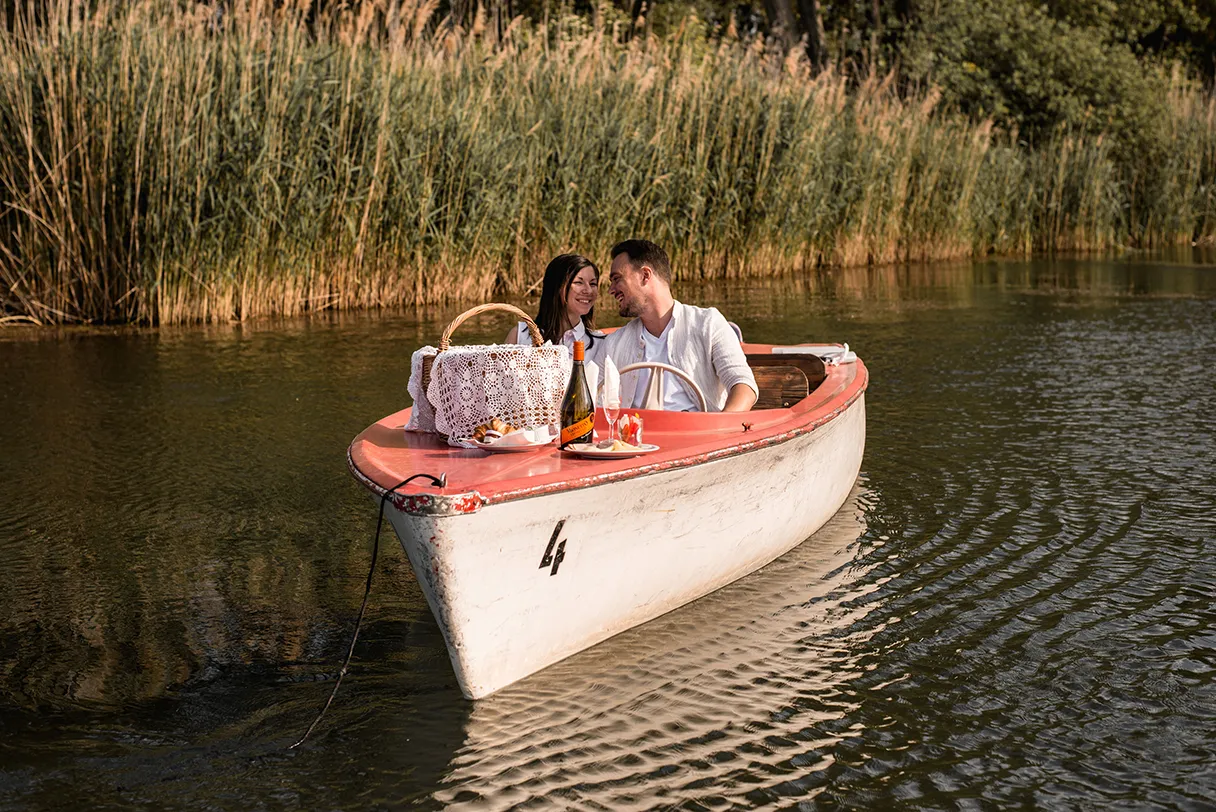 Bootstour mit Wien mal anders. Ein verliebtes Paar sitz in einem Boot und fährt über den See. Im Hintergrund ist grünes Schilf zu sehen.