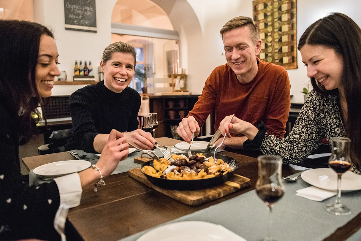 Group of four people sitting at the table enjoying homemade Kaiserschmarrn pancakes
