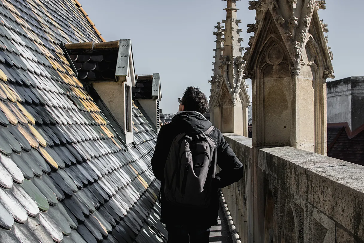 Tour auf den Stephansdom mit Wien mal anders. Man sieht das Dacht des Stephandoms mit den bunten Schindeln. Ein Mann läuft einen schmalen Gang auf dem Dach lang.