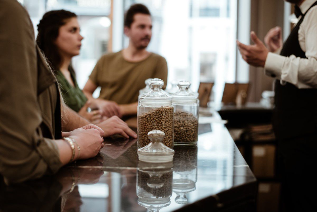 Cafe Hawelka tour with a different Vienna, group standing at the counter and listening, glass with different coffee beans on the counter