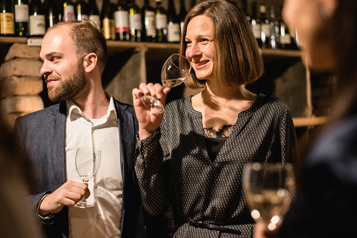 Eine Gruppe bei der Versteckte Weinkeller Tour mit Wien mal anders. Eine Frau hat ein Weinglas in der Hand, der Mann neben ihr guckt zur Seite und lacht.