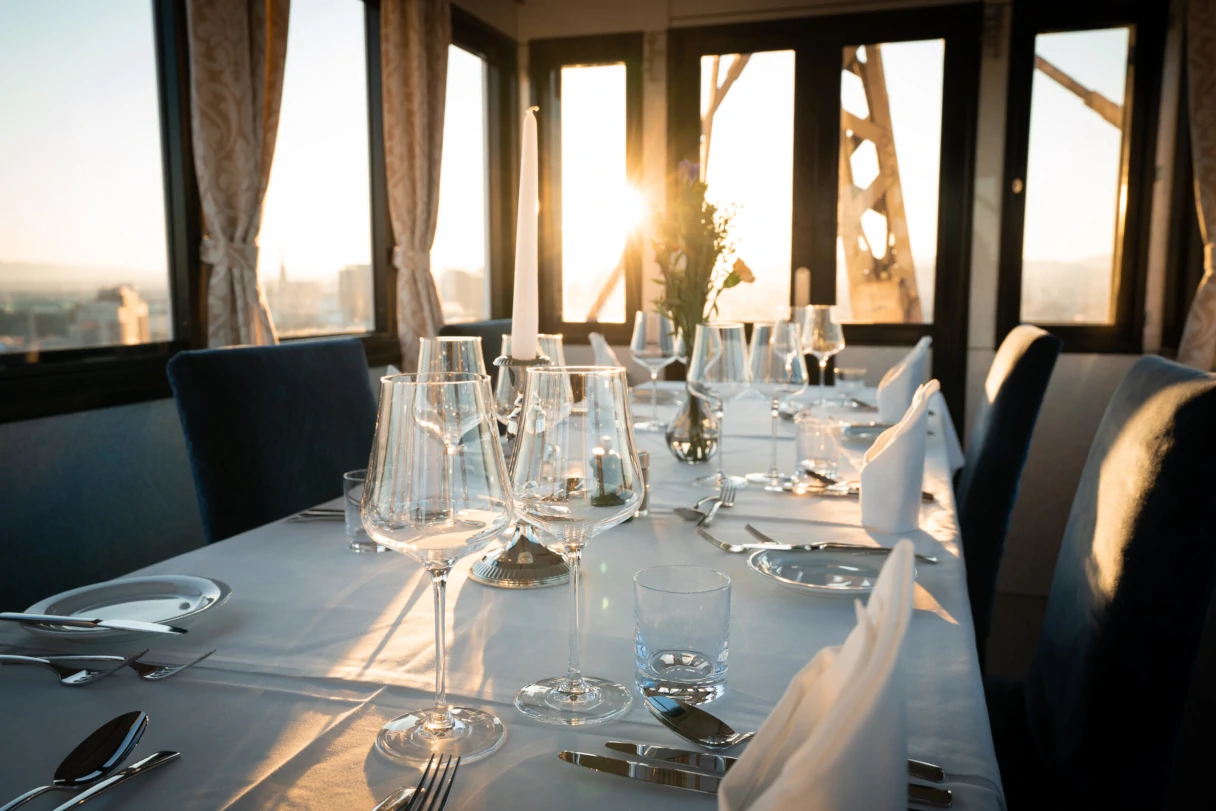 A view inside a dining car on the Vienna Giant Ferris Wheel. The table is set with dishes, glasses, and white napkins. The setting sun shines into the car.