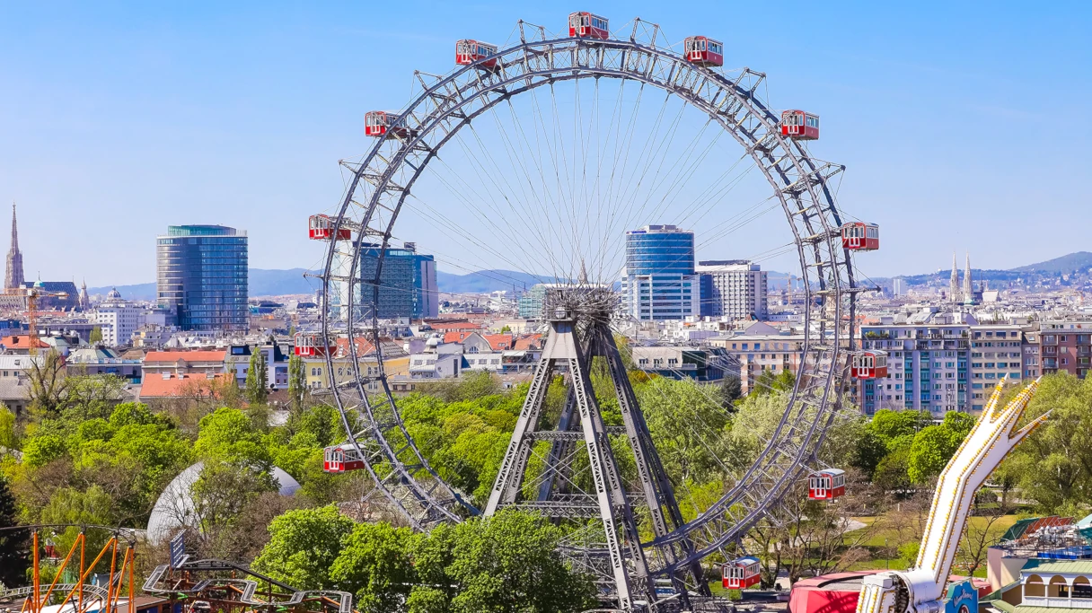 A silhouette of Vienna with the Vienna Giant Ferris Wheel in the foreground. It is a sunny day, and St. Stephen's Cathedral and other Viennese buildings can be seen in the background.