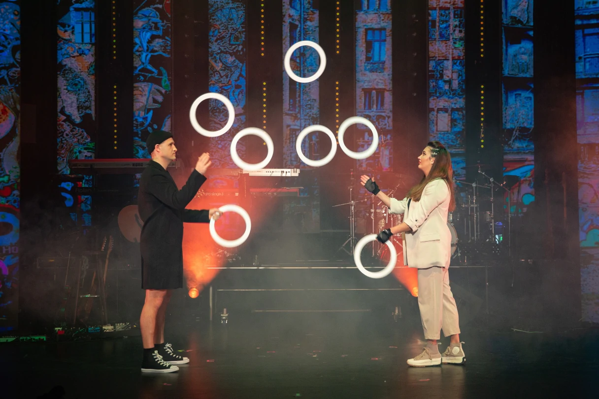 Wintergarten Varieté Berlin, man and woman stand opposite each other on stage and juggle with white rings, red spotlight on stage
